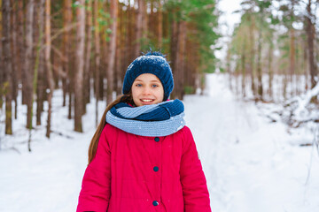 Fototapeta na wymiar Portrait of a little happy girl in winter in a snow-covered hat who walks in the winter forest