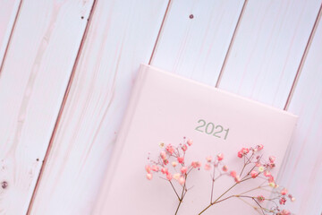 Diary pink organizer with cute pink dried flowers sign 2021 on white pink wooden background.
