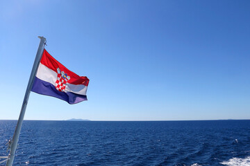 Fototapeta premium Flag of Croatia, blowing in the wind. Adriatic sea and bright sky in the background. Selective focus.