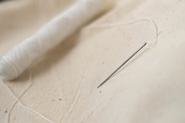 Needle with thread. Spool of thread. Sewing. Sewing machine. Seamstress. Sewing. White threads. Handmade. The cloth.