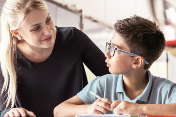 Cheerful school teacher giving help and support to schoolboy in class. Front view. Education or...