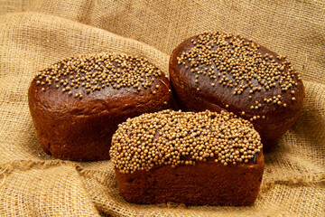 Three loaves of black bread on a burlap background. Fresh aromatic bread.