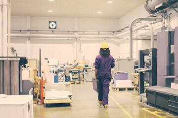 African American female industrial employee in hardhat and overall walking on plant floor. Back view. Work in factory or labor concept