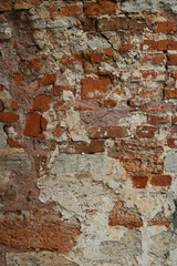 The texture of the old red brick wall. There are asymmetrical cracks  old plaster and repair marks.