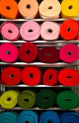 Fototapeta premium Rolls of multi-colored woolen fabric are stacked on racks according to colors. All colors of the rainbow are used.