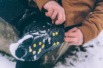 The man has ice shoes on his shoes. A people walks in the snow in winter.