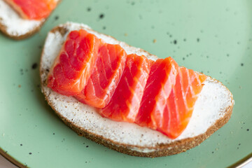 Toast with cream cheese, red fish salmon on a green ceramic plate on a white wooden background, breakfast