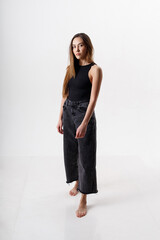 portrait of young attractive asian woman with long hair in black bodysuit, jeans, isolated on white studio background. skinny pretty female posing on cyclorama. model tests of beautiful lady