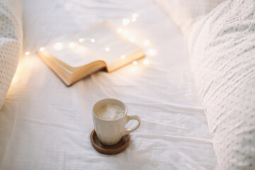 Fototapeta na wymiar Coffee cup with milk foam and a book on a white bedsheet. 