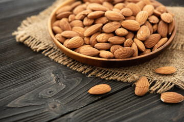 almond in a wooden bowl. on a wooden background, near a bag from burlap. Healthy food and snack, organic vegetarian food. (selective focus; close-up shot)
