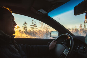 Handsome young man driving in car through winter forest. Closeup photo