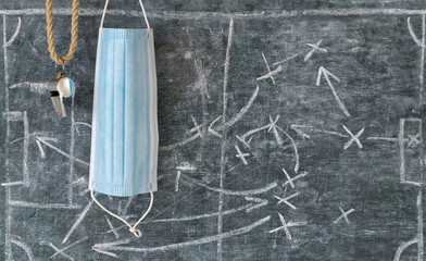 Soccer in times of Coid-19, referee whistle and corona mask on black board with tactical diagram,...