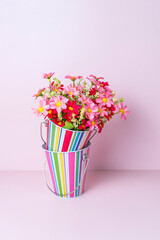  beautiful bouquet of colorful artificial flowers in metal stripes pot isolated on pink background