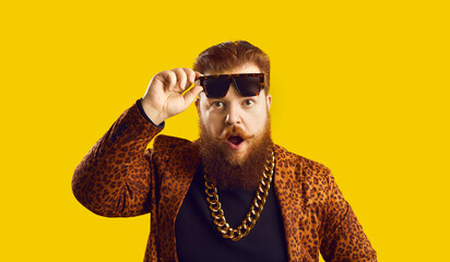 Funny smiling red haired bearded overweight man hipster in leopard jacket and golden chain putting...