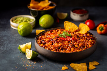 Mexican hot chili con carne in a bowl with tortilla chips on dark background - obrazy, fototapety, plakaty