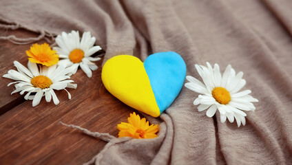 Yellow and blue heart on a rough wooden table with a scarf and daisies. Unity Day, Independence Day of Ukraine, Embroidery Day