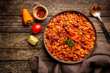 Mexican hot chili con carne in a bowl with tortilla chips on dark background, top view