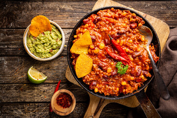 Mexican hot chili con carne in a pan with tortilla chips on dark background, top view