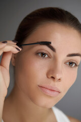 Fototapeta premium Eyebrows shaping. Portrait of beautiful girl with brow pencil. Close-up of young woman with professional makeup contouring brows with eyebrow pencil. Beauty cosmetic concept.