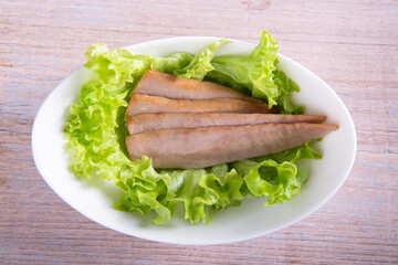 tuna slices with fresh green lettuce in white plate on wooden background flat lay