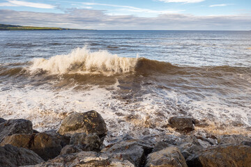 Powerful Atlantic ocean wave hit rough stone coast line. Lahinch town, county Clare, Ireland. Warm sunny day, Majestic cloudy sky. Nature seascape.