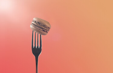 Brown macaroons on a fork. Light pink background. The bokeh effect. Sweetness. Confectionery products. Whipped cream. Dessert.