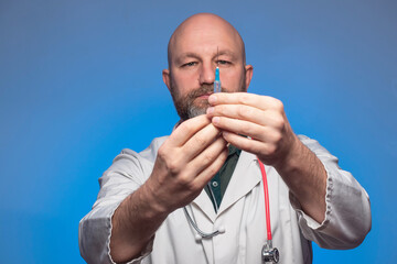 Bald medic in white uniform holding a syringe in his hand. Model in his 40s with beard. Vaccination...