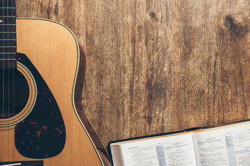 A guitar and a open bible on a wooden background in a dimly lit environment. Soft light and worship