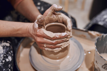 Women working on potters wheel making clay objects in pottery workshop