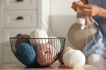 Young woman knitting with needles at home, focus on basket of color threads. Handicraft as hobby