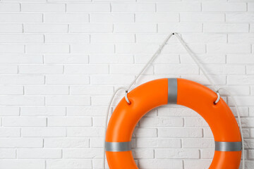 Orange lifebuoy and space for text on white brick wall. Rescue equipment
