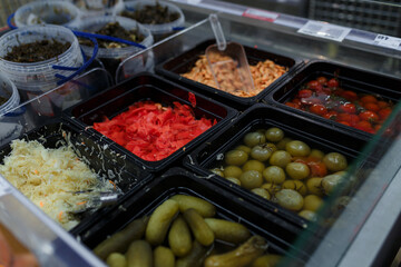 Soft focused shot of vegetable department in grocery store, supermarket, mall, hypermarket or shopping center. Boxes with pickled green and red tomatoes, cabbage, ginger, shrimps and cucumbers.
