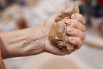 Hand squeezes a piece of clay. Woman preparing clay to make pottery at table in workshop. Handmade Design Art