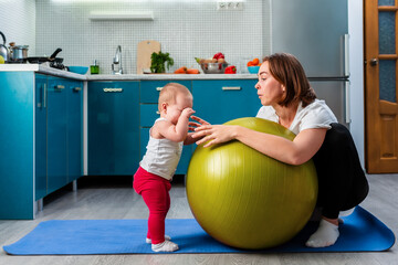 Yoga at home. A young mother leaning on a fit ball, calms her crying baby. The concept of fitness with children at home