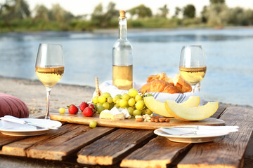 Food for picnic and white wine served on wooden pallet near river