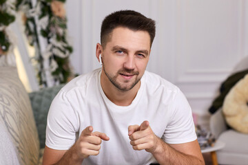 portrait of smiling handsome young man in earphones is talking to somebody on video call at home.