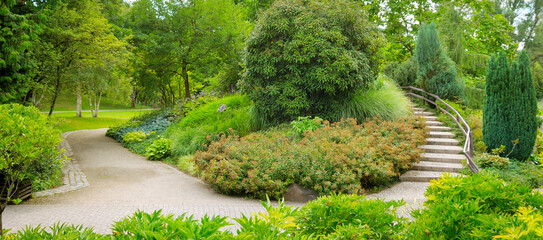 park with beautiful trees, shrubs and a decorative staircase. Wide photo.