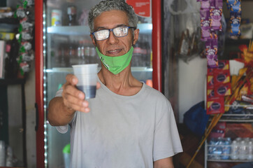 older gray haired latin man working in a shop and cafe offering coffee to customers, giving or distributing coffee with background of sweets