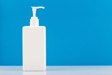 White tall hands sanitizer or alcohol gel bottle with dispenser on white table against blue background with copy space