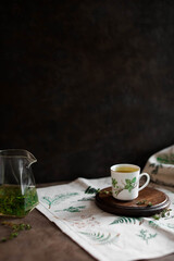 Hot tea with thyme and honey in a small vintage cup. Tablecloth with forest ornament.