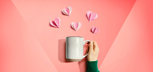 Female hand holding a mug with paper craft hearts - flat lay