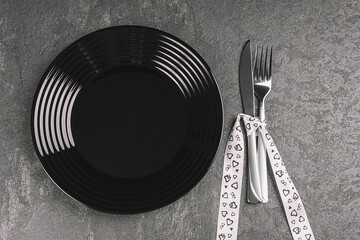 Empty black plate and silverware on black stone table decorated for valentine day