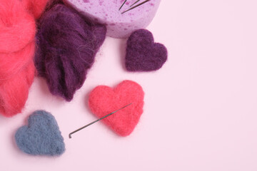 several multi-colored felted woolen hearts on pink background
