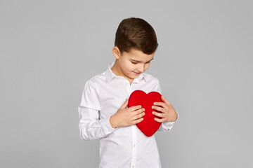 valentine's day. cute little child boy holding red heart isolated on gray background