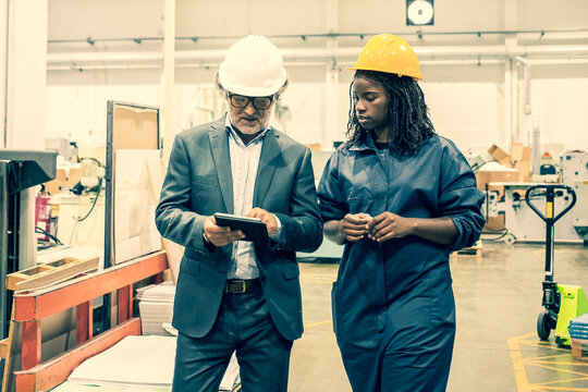 Caucasian manager discussing factory work with African worker. Beautiful pensive young woman working on plant and looking on tablet in supervisor hands. Manufacture and digital technology concept