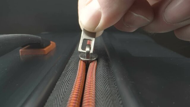 Slowly closing the orange zipper from the luggage bag as seen on a closer look in Estonia