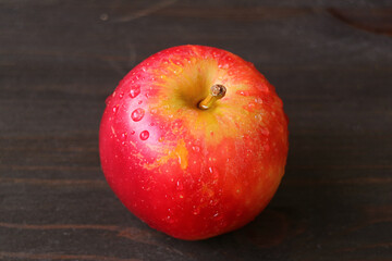 Closeup a fresh ripe red apple with water droplets isolated on dark brown wooden table	