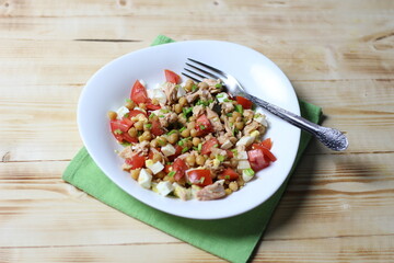 Salad with chickpea, salmon, tomato, egg, green onion, olive oil in white bowl with fork on green textile on wooden background
