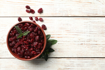 Tasty dried cranberries and leaves on white wooden table, flat lay. Space for text
