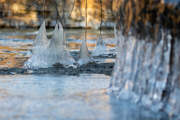 Close-up of icicles hanging from roots, branches and rocks that formed next to a stream.